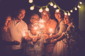 A group of people hold up sparklers underneath a string of lights.