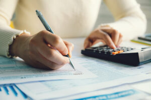 A close-up of a woman filling in her tax return and using a calculator.