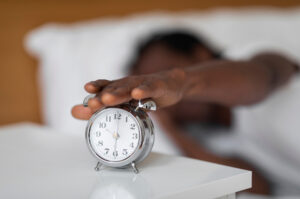 A man lying in bed reaches over to switch off his alarm clock.