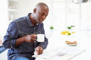 A man drinks a cup of tea while perusing the newspaper at his kitchen table.