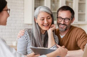 A couple meets with their financial planner who shows them a document on a clipboard.