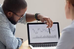 A financial planner points to a graph on a computer monitor in a meeting with his client.