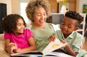 A grandmother sits reading a storybook with her two young grandchildren either side of her.