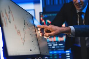 Two stock traders point to a graph on a screen.