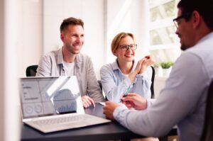 A couple meets with their financial planner who refers to their laptop to offer advice.