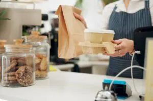 A barista passes a takeaway coffee and brown paper bag over the counter to a customer.